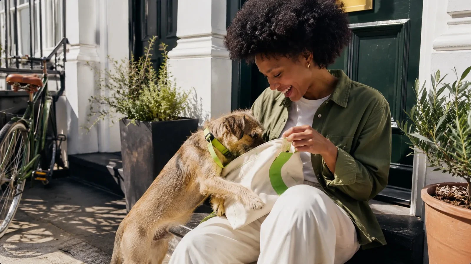 Owner sitting on a London doorstep with a border terrier reaching into her tote bag
